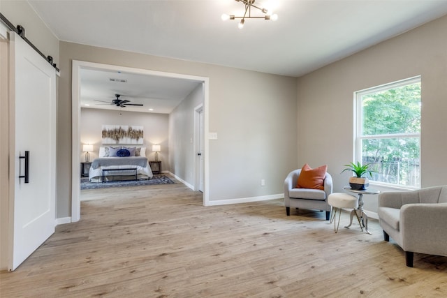 sitting room with ceiling fan, a barn door, and light wood-type flooring