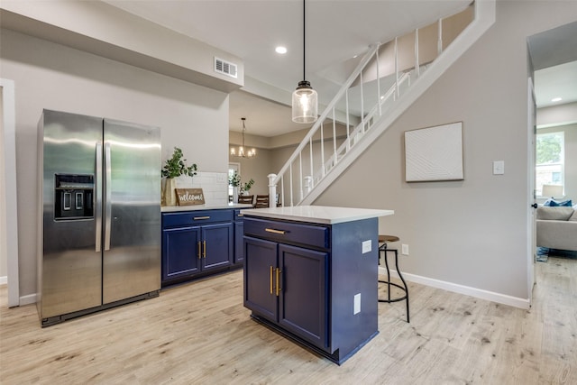 kitchen featuring stainless steel refrigerator with ice dispenser, decorative light fixtures, blue cabinets, a center island, and light wood-type flooring