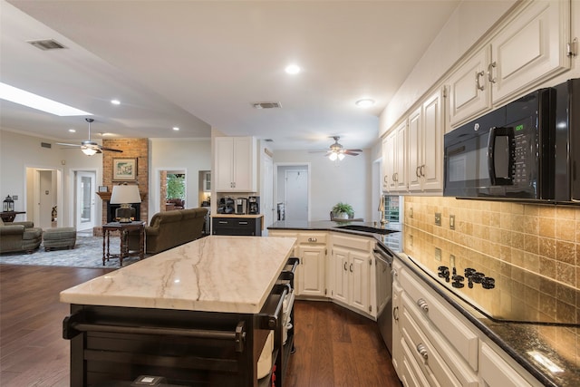 kitchen featuring decorative backsplash, a skylight, stainless steel dishwasher, dark stone countertops, and dark hardwood / wood-style floors