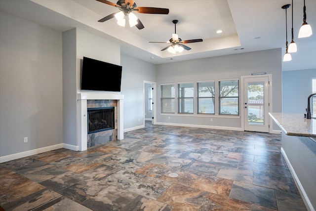 unfurnished living room with a tray ceiling, a tile fireplace, and ceiling fan