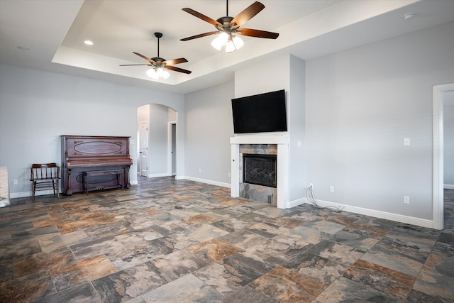 unfurnished living room with a tiled fireplace, ceiling fan, and a tray ceiling