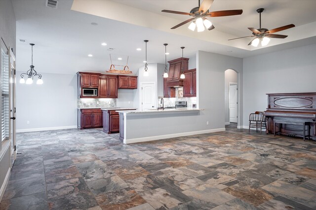 kitchen with stainless steel appliances, tasteful backsplash, a tray ceiling, and decorative light fixtures