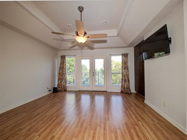 empty room with french doors, a tray ceiling, light wood-type flooring, and ceiling fan