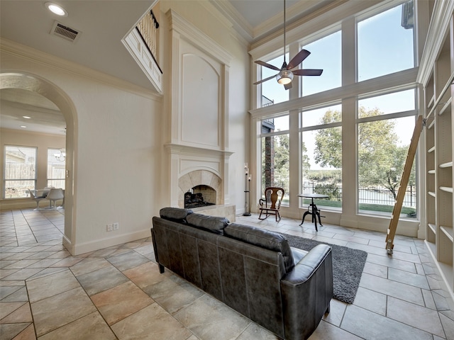 living room featuring crown molding, a healthy amount of sunlight, a towering ceiling, and a tile fireplace