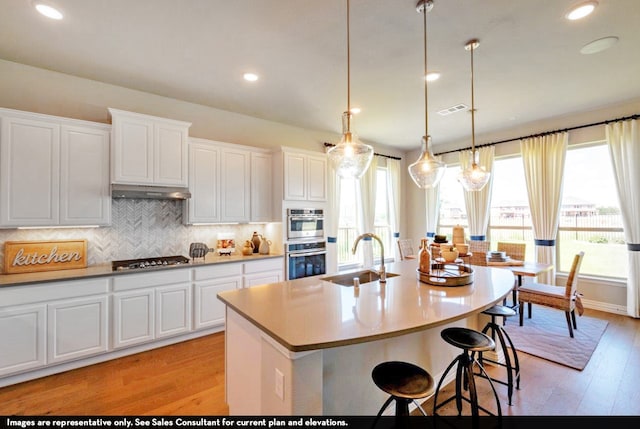 kitchen with sink, an island with sink, light wood-type flooring, and white cabinetry