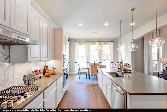 kitchen with a center island with sink, wood-type flooring, stainless steel appliances, decorative light fixtures, and sink