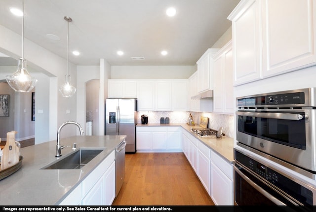 kitchen with hanging light fixtures, stainless steel appliances, sink, white cabinets, and light hardwood / wood-style floors