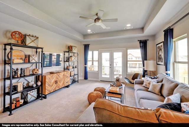 living room featuring a wealth of natural light, french doors, a tray ceiling, and light colored carpet