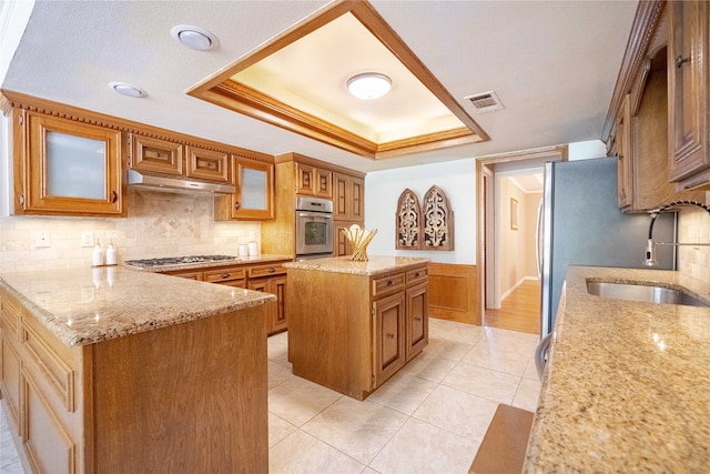 kitchen featuring appliances with stainless steel finishes, sink, a center island, light stone counters, and decorative backsplash