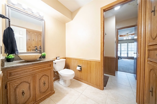 bathroom featuring toilet, ceiling fan, tile patterned floors, wooden walls, and vanity