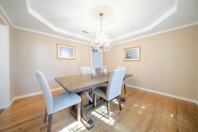 dining space featuring a notable chandelier, light hardwood / wood-style floors, a raised ceiling, and crown molding