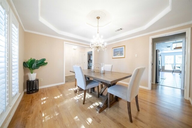 dining space with crown molding, a tray ceiling, light hardwood / wood-style flooring, and an inviting chandelier