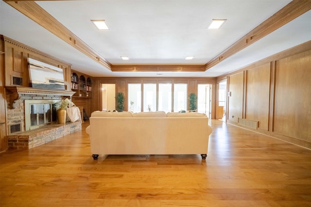 living room with a raised ceiling, light wood-type flooring, and a fireplace