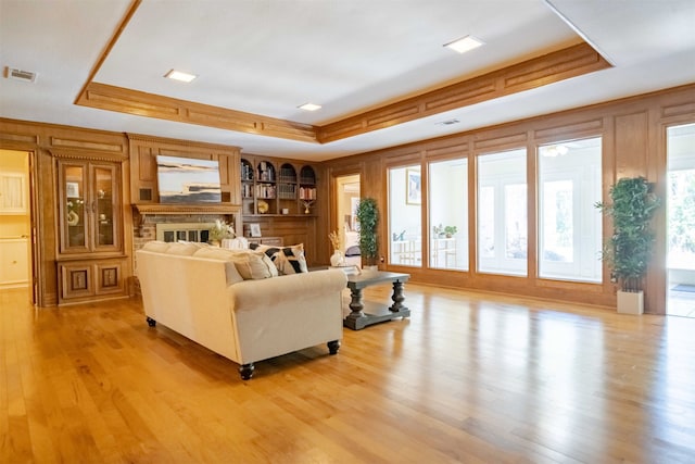 living room with a brick fireplace, light wood-type flooring, and a raised ceiling