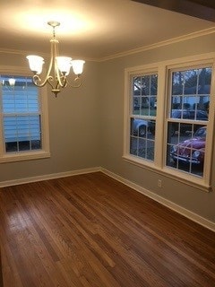 empty room featuring a chandelier, ornamental molding, baseboards, and dark wood finished floors