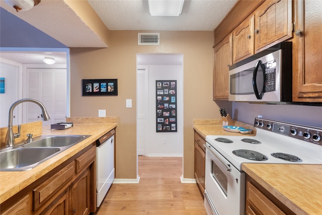 kitchen with white appliances, light hardwood / wood-style flooring, a textured ceiling, and sink