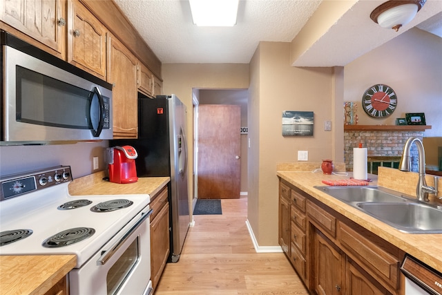 kitchen with sink, appliances with stainless steel finishes, a textured ceiling, and light wood-type flooring