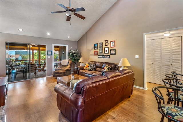 living room with light hardwood / wood-style flooring, a textured ceiling, high vaulted ceiling, and ceiling fan