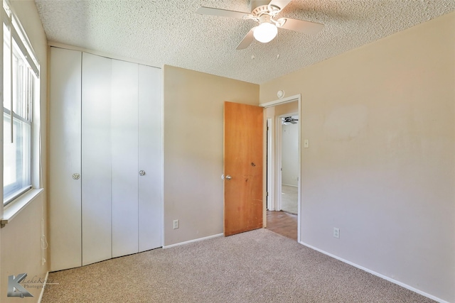 unfurnished bedroom featuring ceiling fan, light colored carpet, a textured ceiling, and a closet