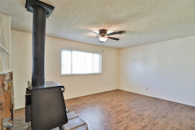 unfurnished living room featuring a textured ceiling, hardwood / wood-style flooring, a wood stove, and ceiling fan