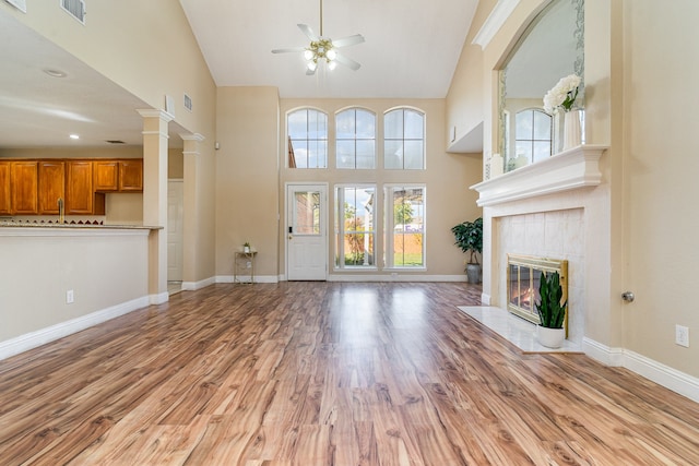 unfurnished living room featuring ceiling fan, a tile fireplace, high vaulted ceiling, and light hardwood / wood-style flooring