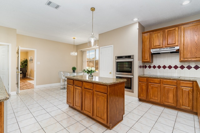 kitchen with stainless steel double oven, light stone counters, pendant lighting, black electric stovetop, and a kitchen island