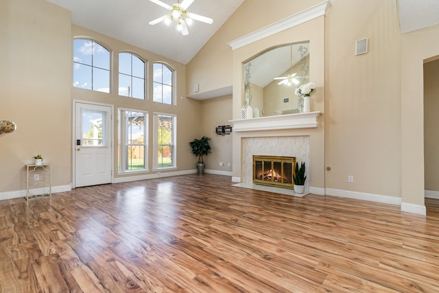 unfurnished living room with a tiled fireplace, ceiling fan, high vaulted ceiling, and light wood-type flooring