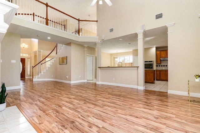 unfurnished living room with ceiling fan with notable chandelier, a towering ceiling, sink, and light hardwood / wood-style flooring