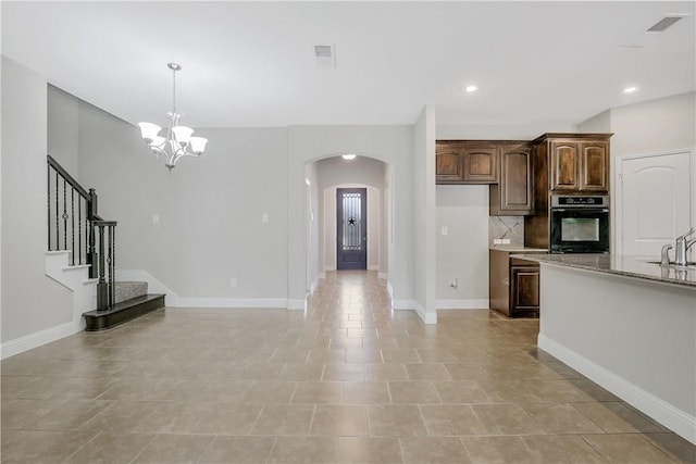 kitchen featuring tasteful backsplash, stainless steel oven, an inviting chandelier, light stone countertops, and dark brown cabinetry