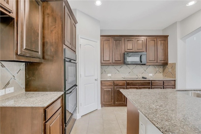 kitchen with light stone counters, black appliances, light tile patterned floors, and backsplash