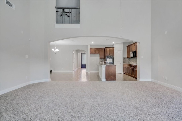 kitchen with an island with sink, black appliances, decorative light fixtures, light colored carpet, and an inviting chandelier