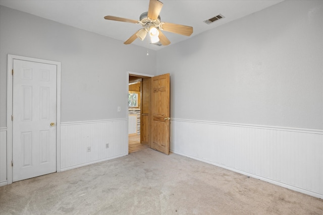 unfurnished bedroom with wooden walls, light colored carpet, and ceiling fan