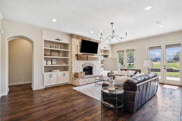 living room with french doors, dark hardwood / wood-style flooring, crown molding, a chandelier, and a stone fireplace