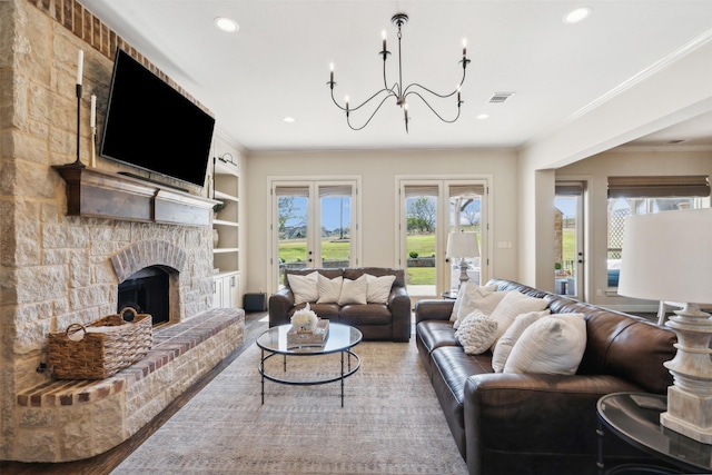 living room with a stone fireplace, built in features, a notable chandelier, wood-type flooring, and ornamental molding