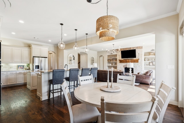 dining area featuring dark wood-type flooring, sink, ornamental molding, built in features, and a fireplace