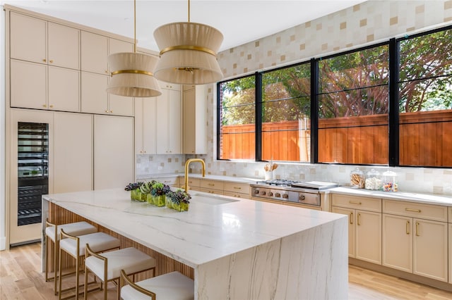 kitchen with pendant lighting, sink, a kitchen island with sink, stove, and beverage cooler