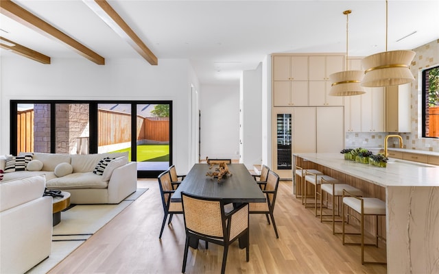 dining room featuring beamed ceiling, light wood-type flooring, and sink