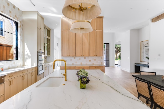 kitchen featuring double oven, light stone counters, backsplash, and a sink