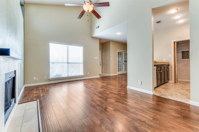 unfurnished living room with ceiling fan, light wood-type flooring, and a high ceiling