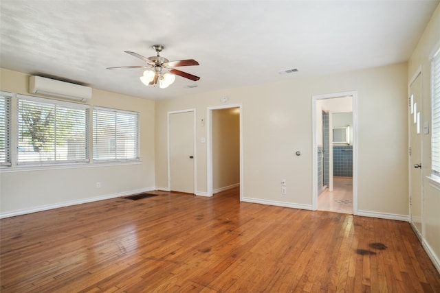 unfurnished room with a wall mounted air conditioner, light wood-type flooring, and ceiling fan