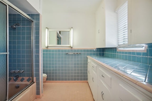 full bathroom with toilet, tile patterned flooring, bath / shower combo with glass door, tile walls, and vanity