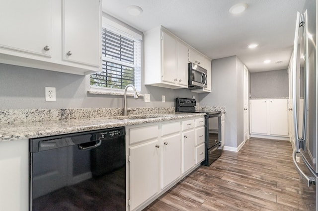 kitchen with black appliances, wood finished floors, a sink, and white cabinetry