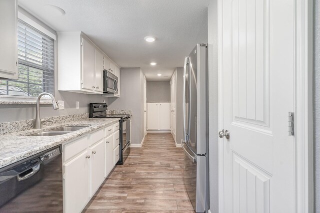 kitchen with a textured ceiling, a sink, white cabinets, light wood-type flooring, and black appliances