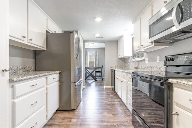 kitchen featuring white cabinets, appliances with stainless steel finishes, a textured ceiling, light wood-type flooring, and a sink