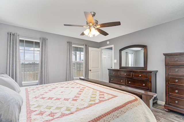 bedroom with ceiling fan, multiple windows, baseboards, and wood finished floors