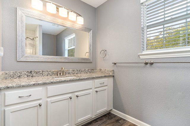 full bath with a healthy amount of sunlight, vanity, baseboards, and wood finished floors