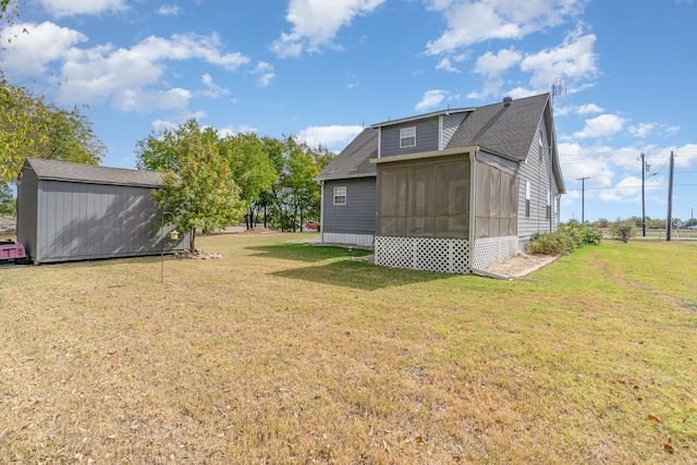 back of property featuring a shingled roof, a sunroom, a lawn, and an outdoor structure