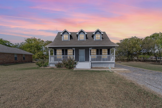 cape cod house featuring covered porch, a shingled roof, and a yard