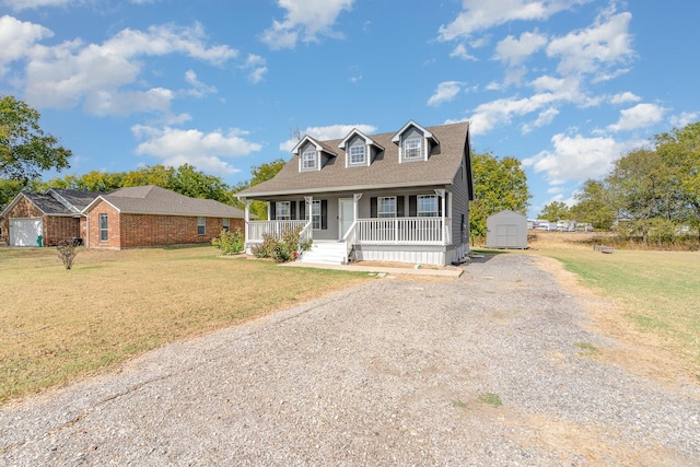 cape cod-style house featuring an outbuilding, a porch, driveway, a shed, and a front lawn