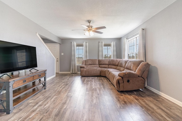 living room featuring a textured ceiling, ceiling fan, wood finished floors, and baseboards